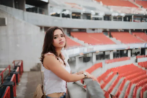 Woman standing in a stadium with a bag on her shoulder, standing in a  stadium, Tiro em Sony A 7 III, inspired by Gina Pellón, standing in an  arena - SeaArt AI