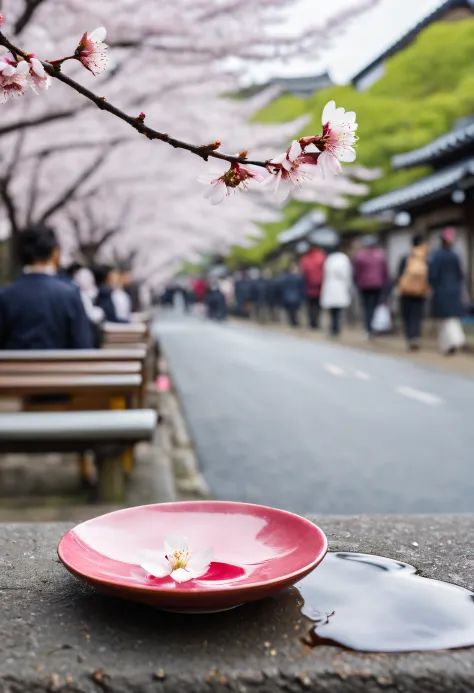 A cherry blossom petal floating on the surface of a sake cup, a woman sitting on a roadside bench, and people walking on the road in the background