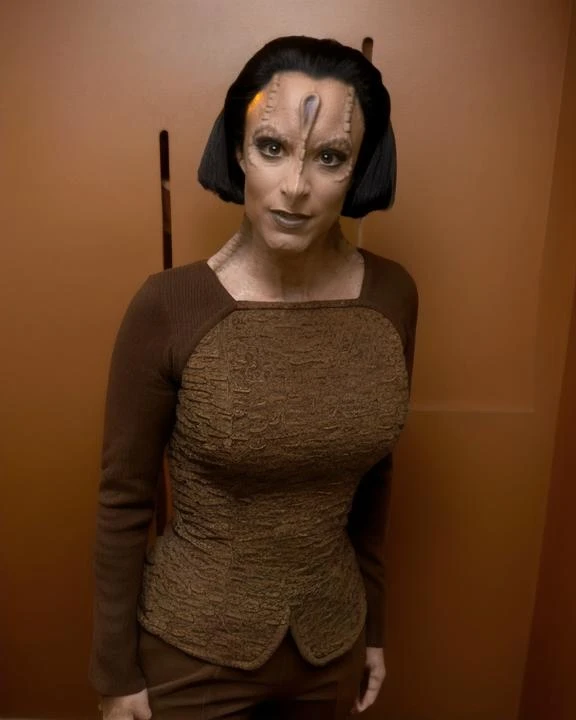 cardassian, female, iliana, grey skin, black swept back updo long hair, wearing greenish brown lipstick, wearing eyeliner, reptile scales on sides of neck, serious expression, wearing brown tunic and brown trousers, wide shot, front view, (raw photo:1.2), fujifilm x100v, standing in a copper colored room, 8k,  visitor, 