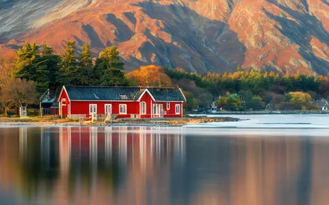 a red house sits on the shore of a lake